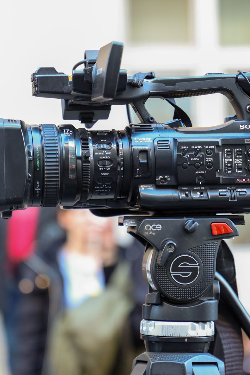 Close-up of a Sony video camera mounted on a tripod for outdoor filming.