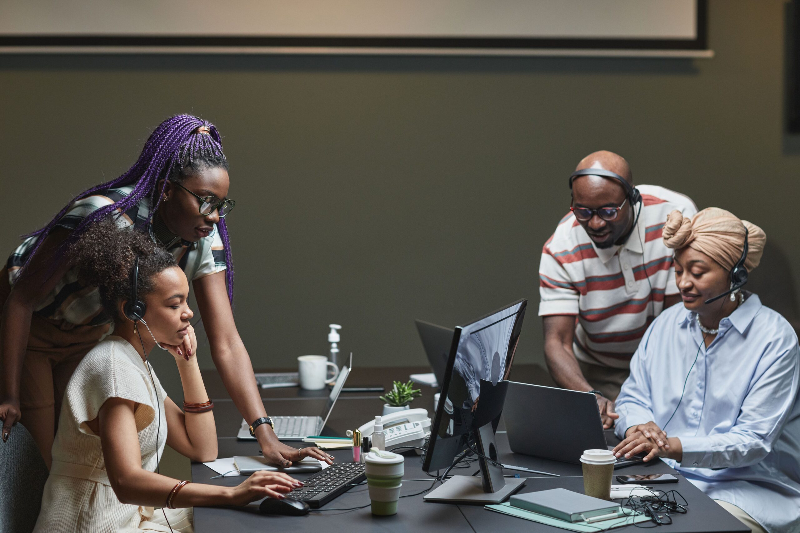 Home A diverse team of professionals collaborating in a modern office environment, using headsets and computers.